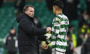 Football manager in black coat and player in green striped jersey shake hands.