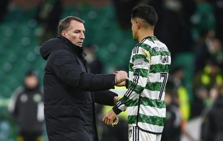 Football manager in black coat and player in green striped jersey shake hands.