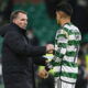 Football manager in black coat and player in green striped jersey shake hands.