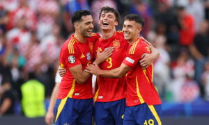 Three footballers in red jerseys embrace.