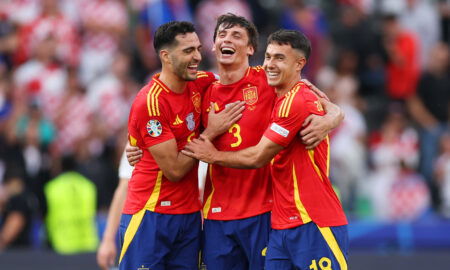 Three footballers in red jerseys embrace.