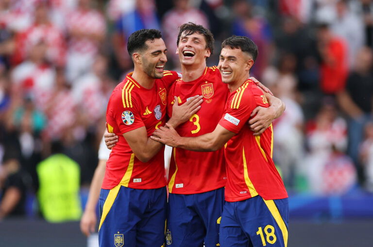 Three footballers in red jerseys embrace.