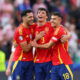 Three footballers in red jerseys embrace.