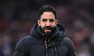 Man with black hair in coat bites tongue.