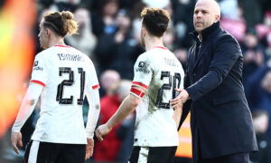 Soccer players in white jerseys consoled by bald manager.