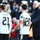 Soccer players in white jerseys consoled by bald manager.