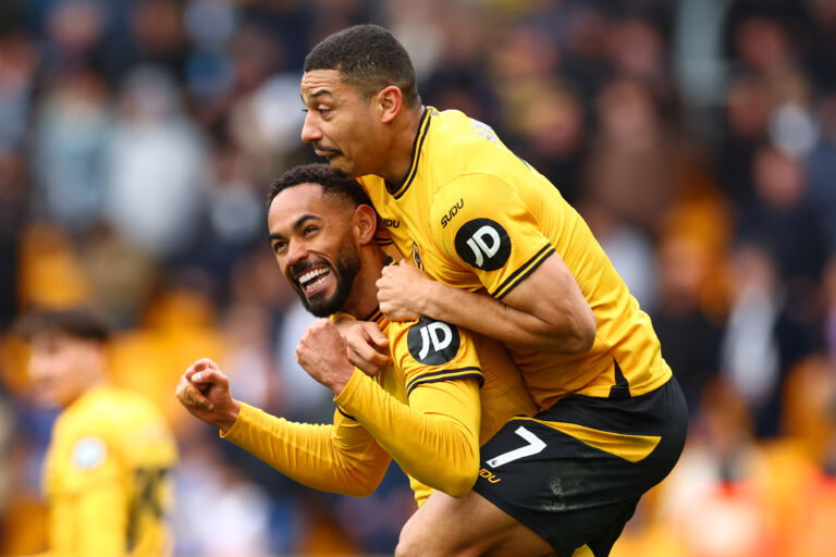 Two soccer players in orange jerseys hug.