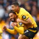 Two soccer players in orange jerseys hug.