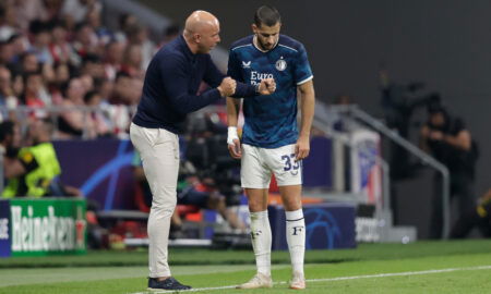 Bald soccer manager coaches player on sideline.