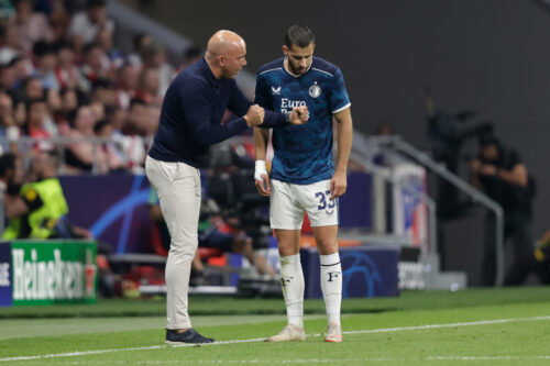 Bald soccer manager coaches player on sideline.