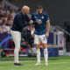 Bald soccer manager coaches player on sideline.