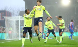 Soccer players in fluorescent yellow jerseys celebrate goal in rain.