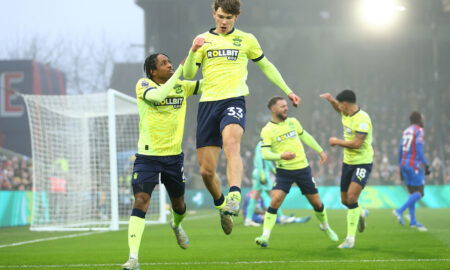 Soccer players in fluorescent yellow jerseys celebrate goal in rain.