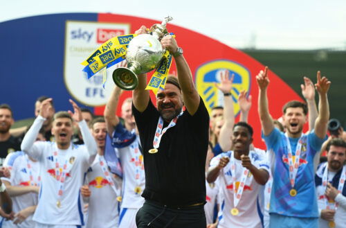 Soccer manager with beard lifts silverware.