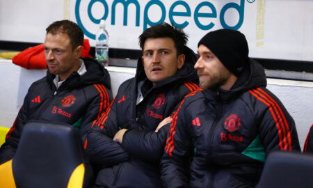 Footballers on bench in coats.