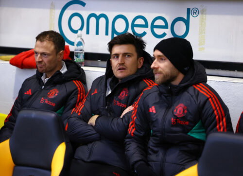 Footballers on bench in coats.