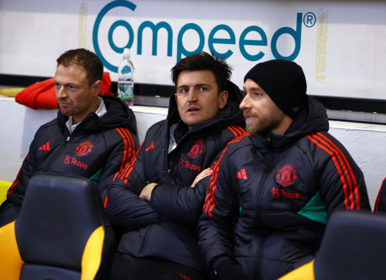 Footballers on bench in coats.