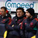 Footballers on bench in coats.